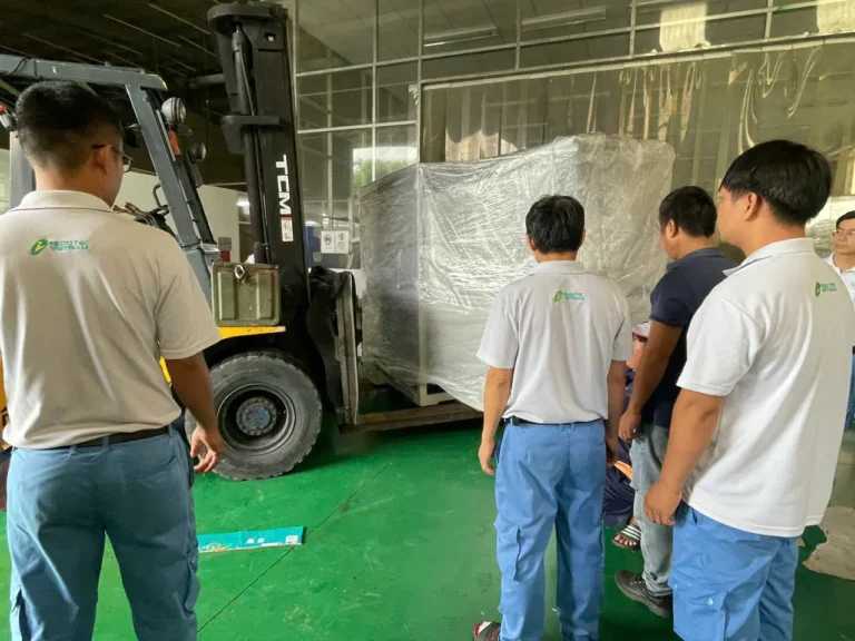 Xe nâng đưa máy đã bọc màng PE ra khỏi xưởng, đội kỹ thuật đứng giám sát quá trình di dời